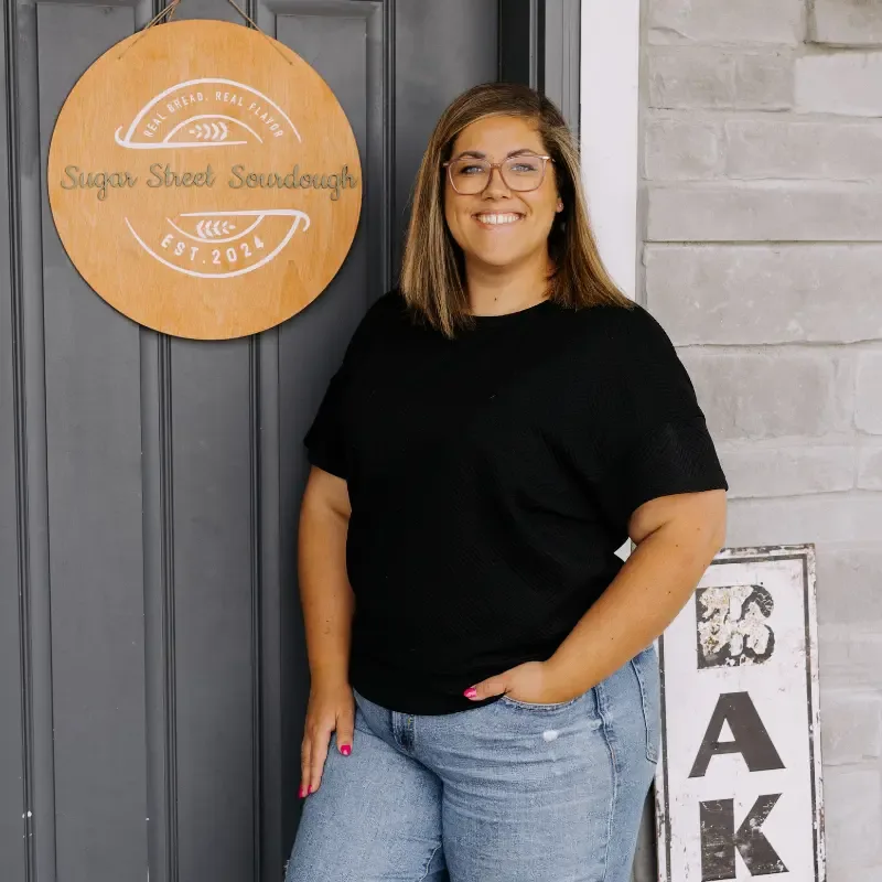 Elise smiling beside the Sugar Street Sourdough sign