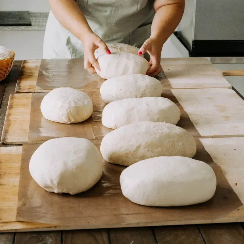 Hands shaping sourdough, with loaves resting on wooden boards